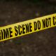 Close-up of crime scene tape with 'Do Not Cross' text, outdoors setting.